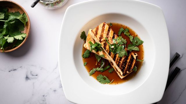 Grilled tofu in a marinade made with soy sauce served in a bowl with cilantro.