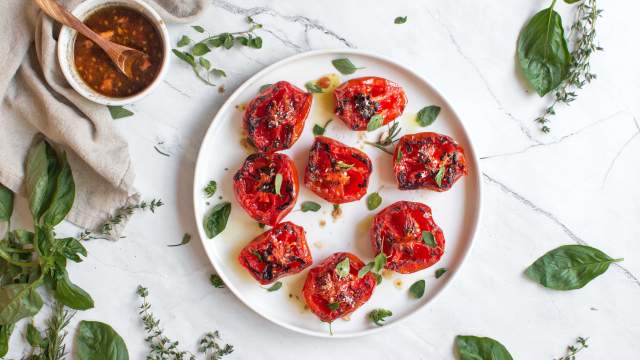 Grilled tomatoes with basil, balsamic vinegar, and garlic on a plate with fresh herbs.