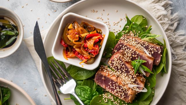 Grilled tuna with soys sauce and sesame seeds on a plate with green onions, lettuce, and cooked peppers.