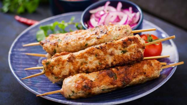 Grilled turkey lula kabobs with red onions, parsley, and lemon on a slate board.