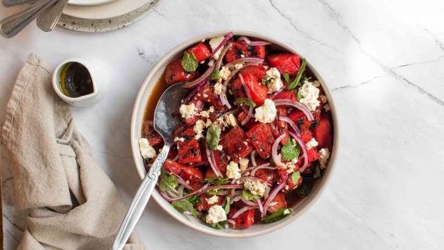 Grilled watermelon salad with feta cheese, fresh mint, basil, red onion, and balsamic vinegar in a bowl. 