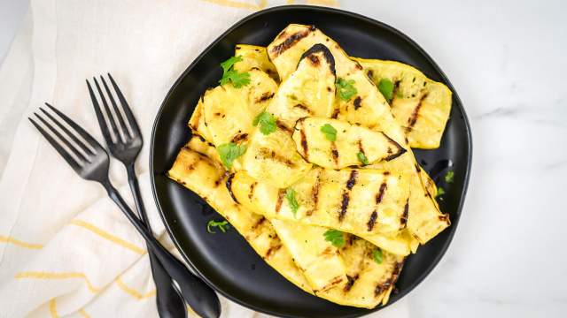 Grilled yellow squash on a black plate sprinkled with parsley.