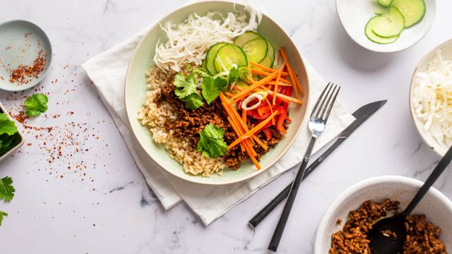 Ground beef bulgogi bowls with Korean flavored beef, cucumbers, carrots, red peppers, cabbage, and rice in a bowl. 