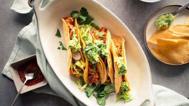 Ground turkey tacos in crispy baked tortillas with salsa, lettuce, radishes, and guacamole on a plate.