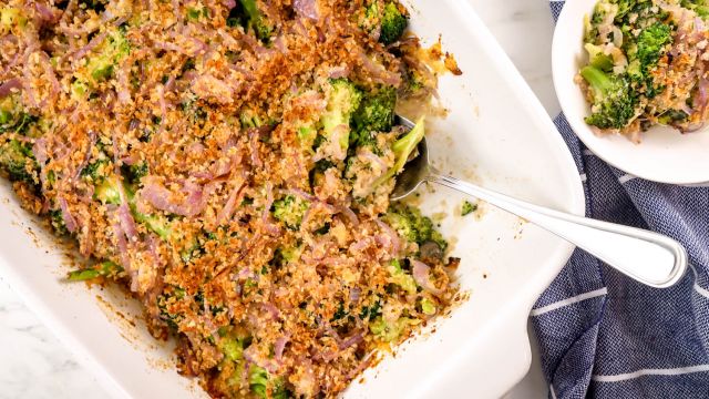 Healthy broccoli casserole with mushrooms, cheddar cheese, and crispy onions in a baking dish with a spoon.