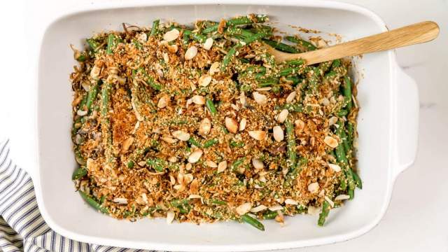 Healthy Green Bean Casserole with green beans, mushroom sauce, and a crispy almond onion topping in a baking dish with a striped napkin.