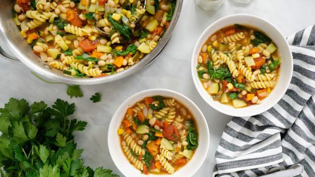 Minestrone soup with zucchini, yellow squash, pasta, white beans, spinach, and tomatoes in two bowls. 