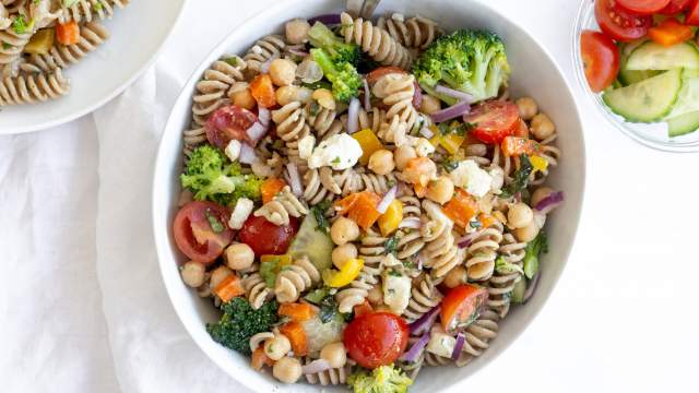 Vegetable pasta salad with cooked whole wheat pasta, chopped fresh vegetables, chickpeas, and feta cheese topped with lemon dressing.