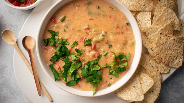 Healthy queso dip with melted cheddar cheese, diced tomatoes, and jalapeños in a bowl with tortilla chips.