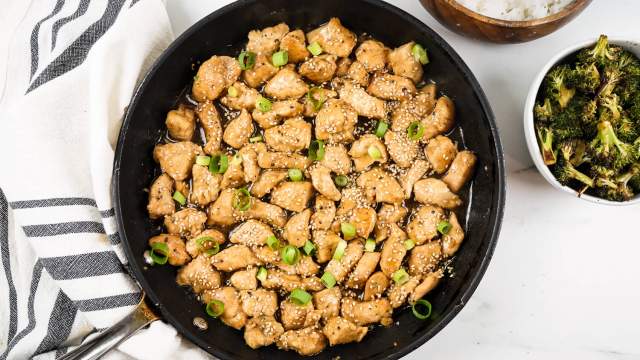 Healthy Sesame Chicken in a skillet with green onions with white rice and broccoli on the side.