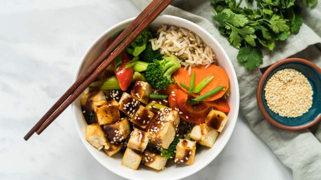 Hoisin tofu with broccoli, carrots, peppers, and green onions over brown rice with hoisin sauce drizzled on top.