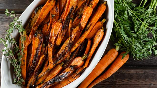 Honey Balsamic Carrots in a white dish with fresh carrots on the side.