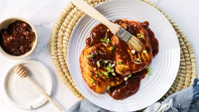 Honey chipotle grilled chicken on a plate with sliced green onions and honey chiptole sauce.