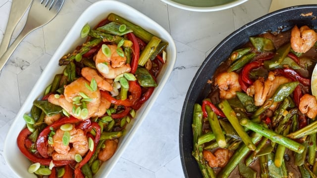 Honey garlic shrimp stir fry on a plate with asparagus, snap peas, red peppers, and stir fry sauce.