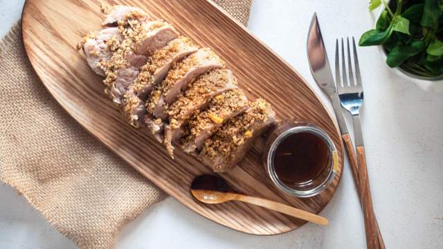 Honey pork tenderloin coated with sesame seeds sliced on a wooden board with a soy garlic marinade on the side.