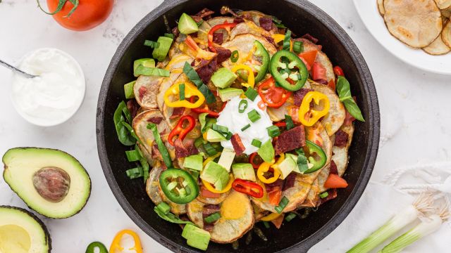 Irish Nachos with crispy baked potato chips, bacon, cheese, avocado, peppers, and sliced green onions in a cast iron skillet.