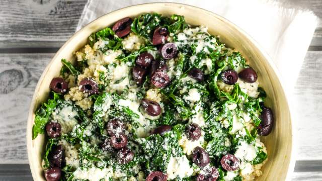 Kale caesar quinoa bowl with shredded kale, cooked quinoa, creamy Caesar dressing, and black olives in a wooden bowl.