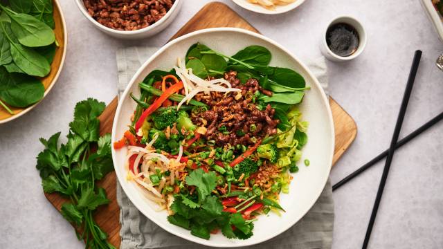 Korean beef bowls with rice, cilantro, carrots, bell peppers, and sprouts in a bowl with spicy sauce. 