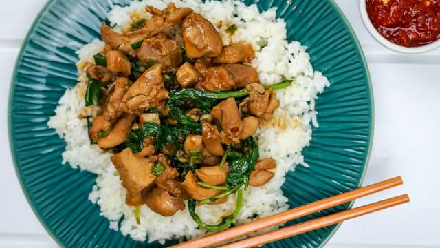 Korean chicken with spinach, rice, and hot sauce on a plate with chopsticks.