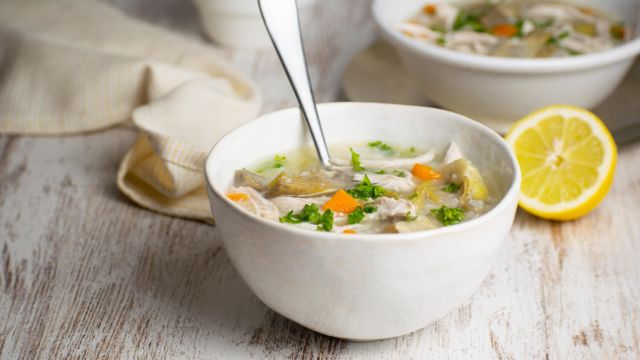 Slow cooker lemon artichoke chicken soup with quinoa in a bowl with carrots and lemon.