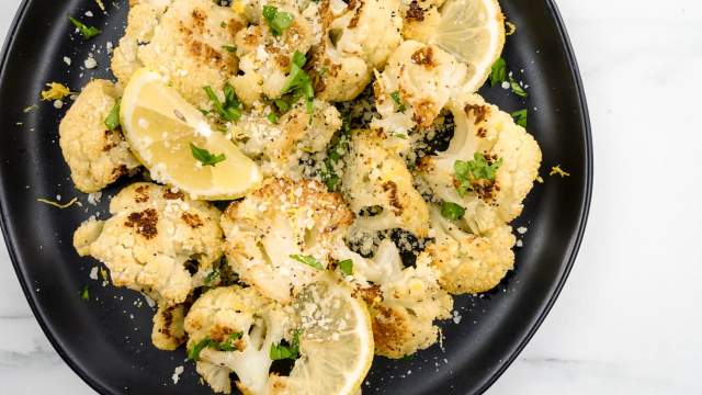 Lemon garlic roasted cauliflower with Parmesan cheese and lemon slices on a black plate.