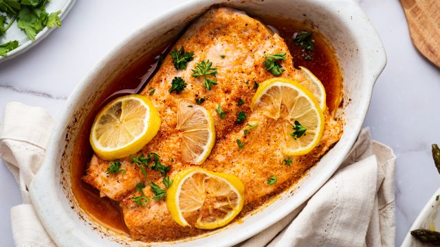 Lemon pepper salmon with slices on lemon and parsley in a white baling dish.