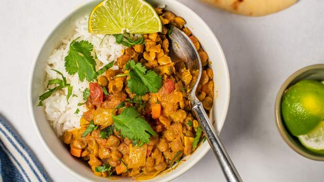 Lentil coconut curry in a white bowl with creamy lentils, carrots, and tomatoes in a creamy coconut broth with rice.