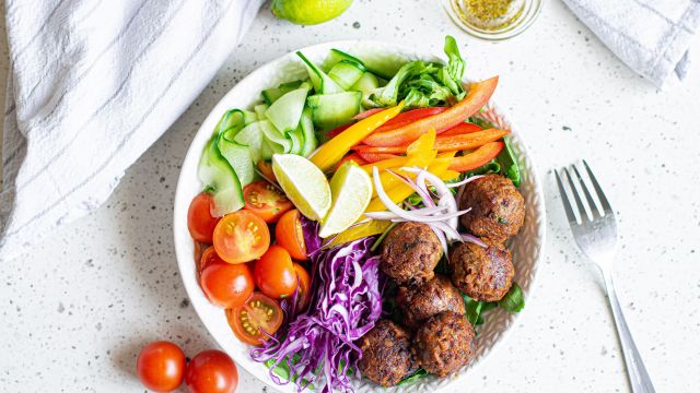 Lentil meatballs served in a bowl with cabbage, peppers, tomatoes, cucumber, red onion, and limes.