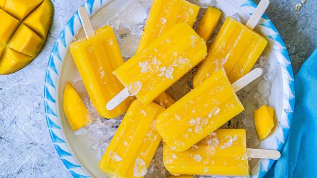 Mango popiscles made with fresh mango pieces, lime juice, water, and honey on a plate with ice.