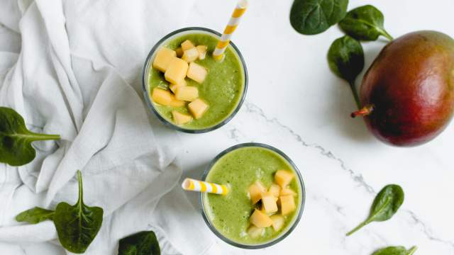 Mango spinach smoothie in two cups with fresh mango chunks on top.