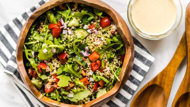 Mediterranean quinoa bowl with quinoa, arugula, red peppers, tomatoes, and hummus dressing in a wooden bowl.