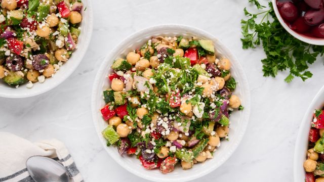 Mediterranean salad with chickpeas, olives, bell peppers, fresh herbs, and feta cheese in a bowl.