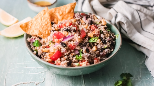 Mexican quinoa with black beans, corn, tomatoes, onion, taco seasoning, and cilantro served in a bowl with chips.