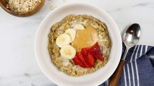 Banana Peanut Butter Microwave Oatmeal in a bowl with rolled oats, bananas, peanut butter, and strawberries.