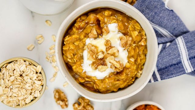 Pumpkin oatmeal with walnuts, maple syrup, and yogurt in a bowl with oats on the side.