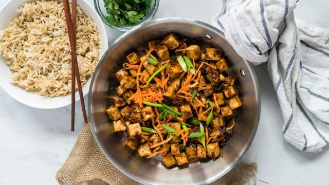 Mongolian tofu in a skillet with carrots, green onions, crispy tofu, and a sweet and spicy sauce.