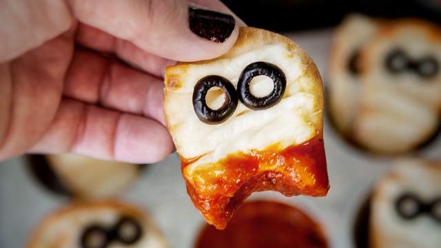 Mummy pizza flatbread being held above a muffin tray with marinara sauce for dipping.