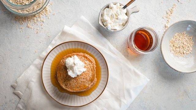 Oatmeal protein pancakes made with rolled oats, egg whites, and cottage cheese stacked on a plate with maple syrup and whipped cream.