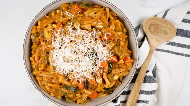 One pot creamy vegetable pasta with tomato sauce in bowl with mozzarella cheese.