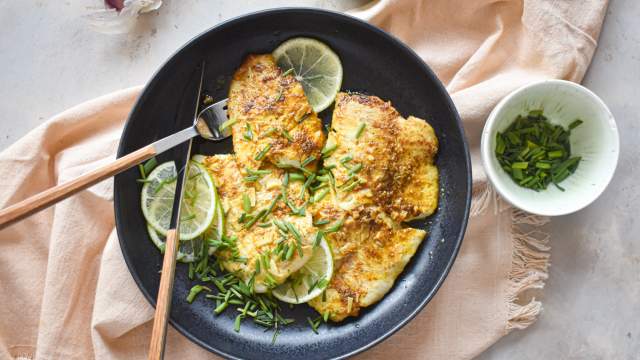 Pan fried garlic lime tilapia on a plate with fresh limes, green onions, and garlic.