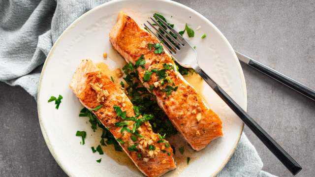 Pan seared salmon with garlic, lemon, and butter served on a plate with a lettuce and tomato salad.