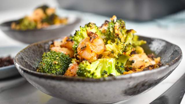 Garlic Roasted shrimp and broccoli in a bowl with shredded cheese, lemon, and red pepper flakes.