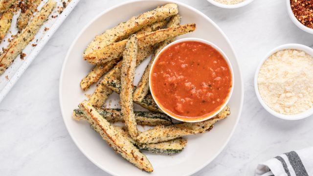 Baked Parmesan zucchini fries with a crispy panko breading on a white plate with marinara sauce.