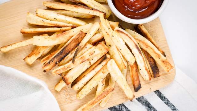 Parsnip fries cut into match sticks with spices on a wooden cutting board with kethcup.