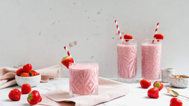 PB&J Smoothie with Greek yogurt in three glasses with fresh strawberries and peanut butter on the side.