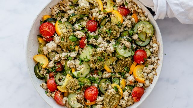 Ground turkey, zucchini, yellow squash, and cherry tomatoes in a skillet and topped with pesto.