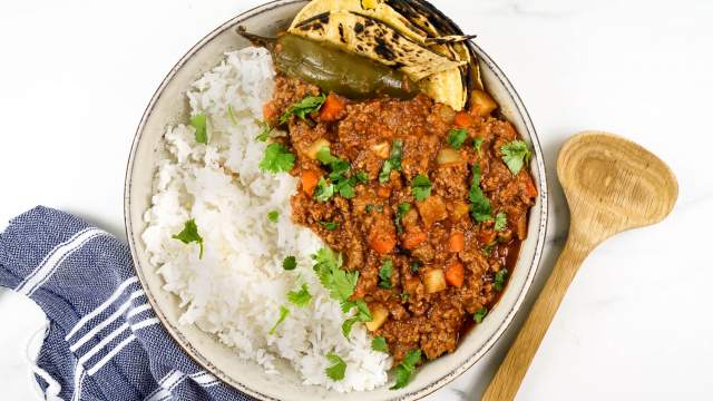 Picadillo with potatoes, carrots, and chipotle tomato sauce in a bowl with rice, tortillas, and cilantro.