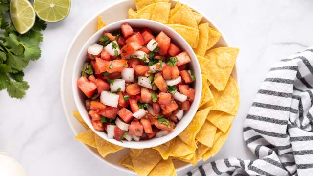 Pico de gallo with diced tomatoes, white onion, cilantro, jalapeno, and lime juice in a white bowl with tortilla chips on the side.