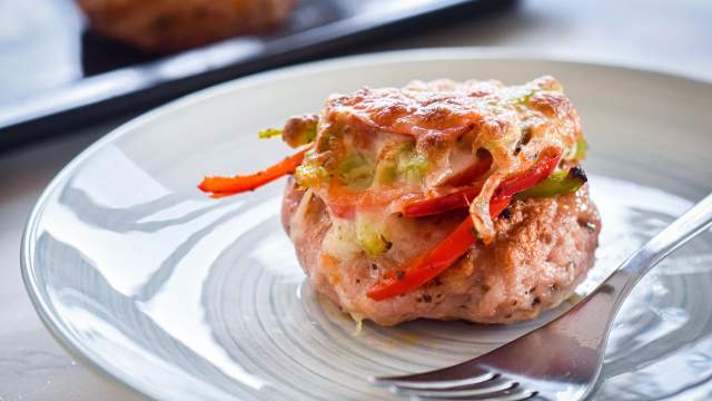 Pizza turkey burgers with marinara sauce, melted cheese, peppers, onions, and basil on a plate with a fork.