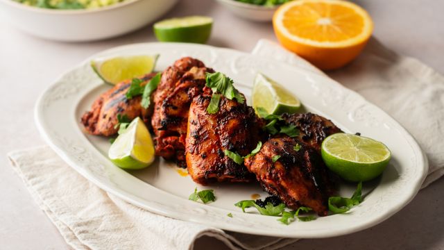 Pollo asado made with chicken thighs marinated in achiote paste and citrus juice served on a plate with guacamole and pickled onions.